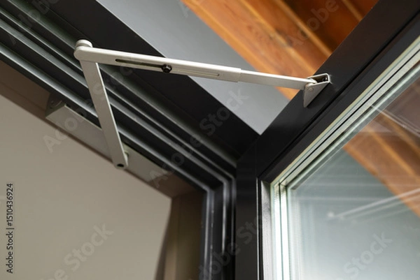 Fototapeta Close-up of a modern door closer mechanism in an open aluminum-framed window, showing construction detail and engineering design.