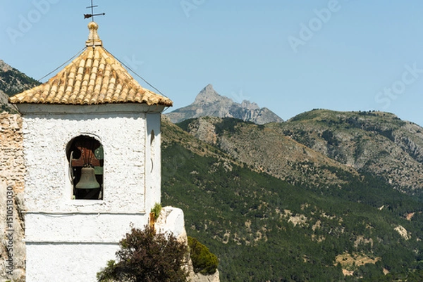Obraz Historic bell tower stands against green mountain background. Image suitable for travel, architecture, or heritage concepts.