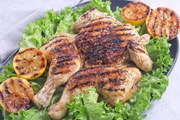 Fototapeta Grilled spatchcocked chicken with lemon garlic marinade on lettuce with lemon halves, horizontal