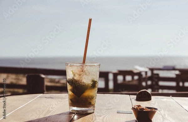 Obraz Chilled mojito served with a straw with the ocean in the background.
