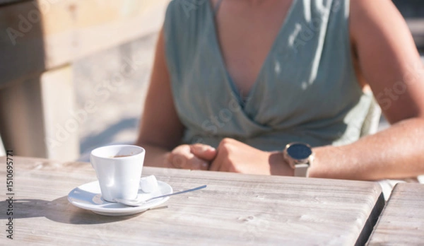 Obraz Beautiful young woman enjoying an espresso served on a terrace with the ocean in the background.