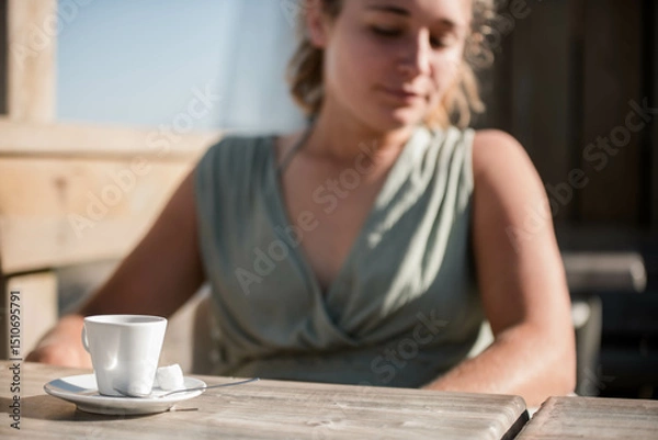 Obraz Beautiful young woman enjoying an espresso served on a terrace with the ocean in the background.
