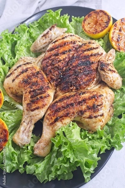 Fototapeta Grilled spatchcocked chicken with lemon garlic marinade on lettuce with lemon halves, vertical