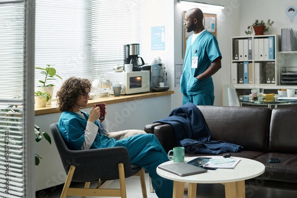 Fototapeta Medical professionals sitting and standing in hospital lounge during break. Relaxing atmosphere with coffee machine, plants, and ample seating creating a welcoming space for staff