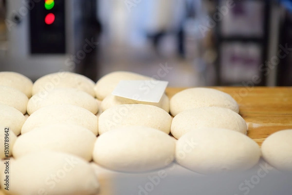 Fototapeta A batch of formed dough pieces on a table in the kitchen of a local bakery ready to bake. Olive ciabatta blanks laid out in a row in front of a large oven. Local bread production