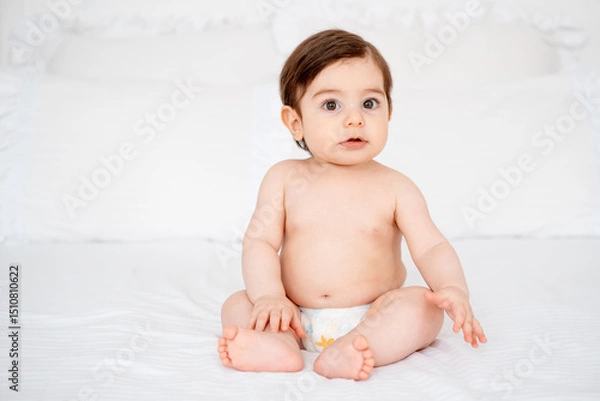 Fototapeta A baby in diapers on a white bed at home, a place for text, a cute smiling little child