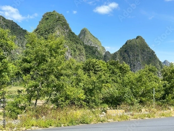 Obraz A stunning vista unfolds, displaying verdant mountains, trees, and clear skies under sunlight in Guangxi, China.