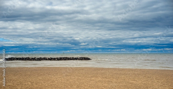 Fototapeta A section of a beach on Lake Erie at Presque Isle State Park, Pennsylvania, with a breakwater and a tiny sailing ship visible on the horizon