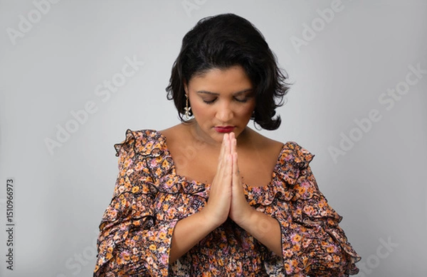 Fototapeta Horizontal portrait of woman looking down with hands in prayer position. Perfect for religion, gratitude, belief, faith themes. Studio shot with copy space on gray background.