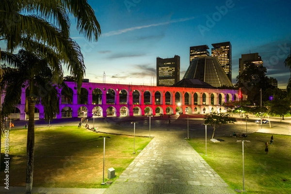 Fototapeta Lapa Aqueduct Illuminated With Purple and Pink Colors in the Evening With Tall Office Buildings of Rio de Janeiro Downtown