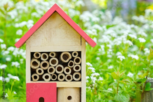 Fototapeta An insect hotel or bee hotel in a summer garden with flowers. An insect hotel is a manmade structure created to provide shelter for insects in a variety of shapes and sizes and materials.	