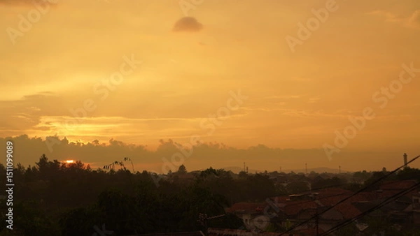Fototapeta Golden Sunset Over a City with Silhouetted Trees and Rooftops