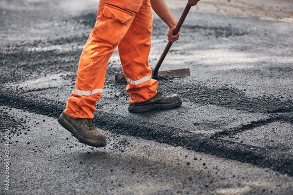 Fototapeta Construction worker working on a new asphalt layer on a public street.
