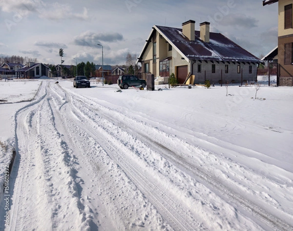 Fototapeta Snow covered, uncleared road in a siberian cottage village after Spring snowfall.