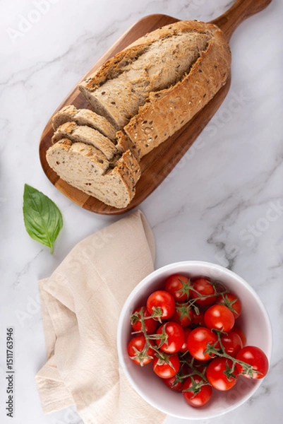 Obraz Top view of whole grain bread on wooden board with cherry tomatoes and basil on light marble background. Healthy and Mediterranean food. Concept of healthy breakfast and natural lifestyle