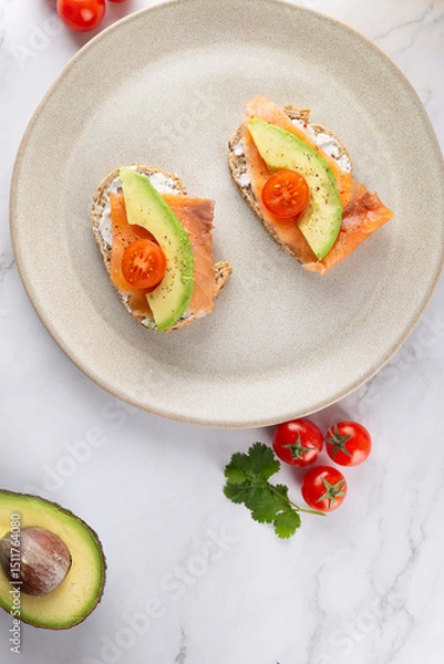 Obraz Top view close-up of two toasts with avocado, salmon and cherry tomatoes on beige plate. White marble background. Concept of healthy breakfast and balanced nutrition