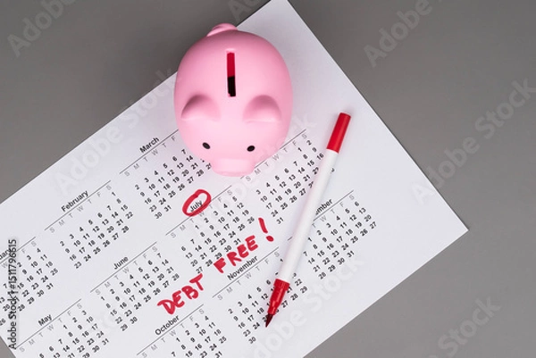 Fototapeta Piggy bank on calendar with the words 'Debt Free' written on it, symbolizing saving money, financial freedom, and achieving a debt-free lifestyle. Concept of financial independence and budgeting.