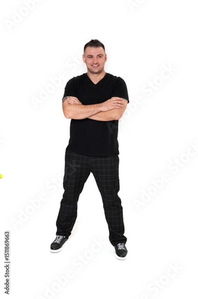 Obraz A handsome dark-haired man in a black T-shirt, trousers and sneakers on a white background