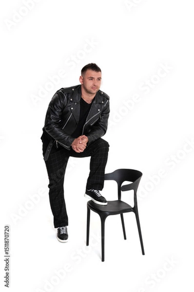 Obraz A handsome dark-haired man in a black leather jacket, black T-shirt, trousers and sneakers on a white background