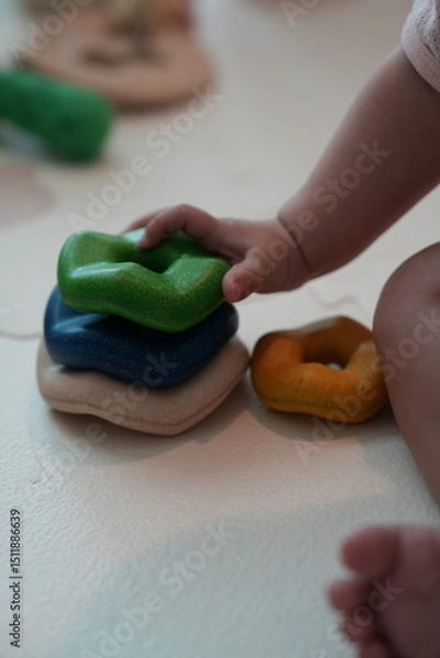 Fototapeta A baby"s hand stacks colorful, irregularly shaped toys on a light surface, promoting sensory play and early childhood development.