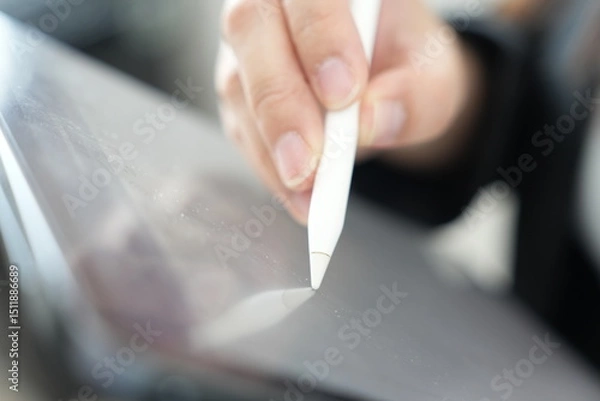 Fototapeta A hand using a digital stylus to write or draw on a tablet screen.