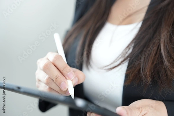 Fototapeta A businesswoman uses a digital pen on a tablet, focusing on modern, professional technology in a workplace setting.
