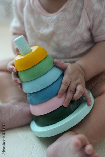 Fototapeta A baby playing with a colorful stacking ring toy while sitting on the floor.