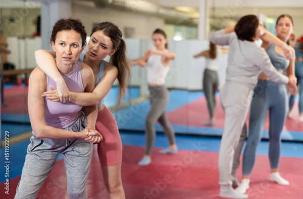 Fototapeta Women train to perform effective blows and impact on pain points while learning self-defense techniques. Contact with opponent in self defense combat..