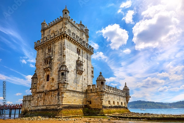 Fototapeta Lisbon, Portugal. Tower Belem at coast of river Tagus. Stones and mussels day during low tide. Sunny blue sky with clouds.