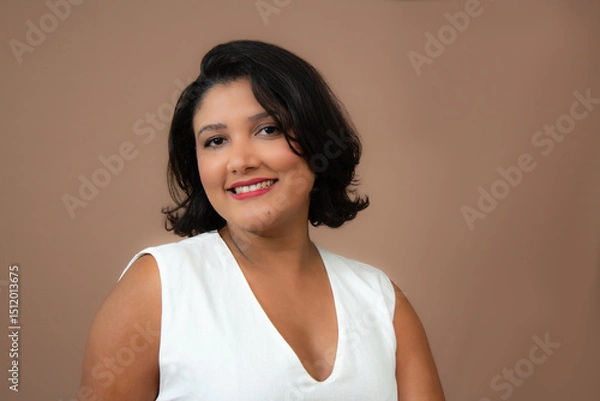 Fototapeta Charming businesswoman in white top smiling at camera. Perfect for professional development,  soft skills, career, personal growth. Horizontal studio portrait with copy space on brown background.