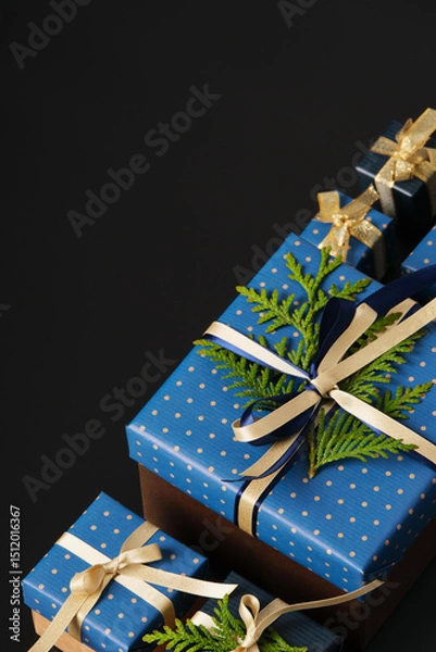 Obraz Selective focus wrapped gifts decorated with blue polka dot paper, gold ribbons and sprigs of fresh greenery on a black background. Space for your text