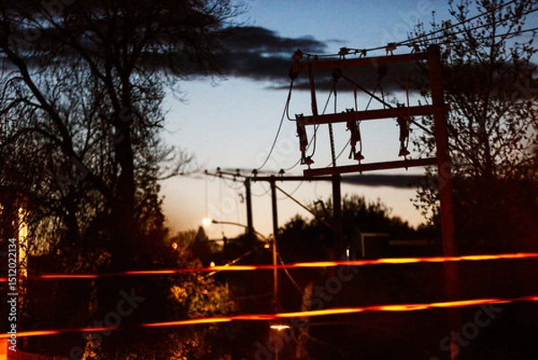 Fototapeta Pylônes et fils électriques dans la lumière du soir au coucher du soleil en ville.