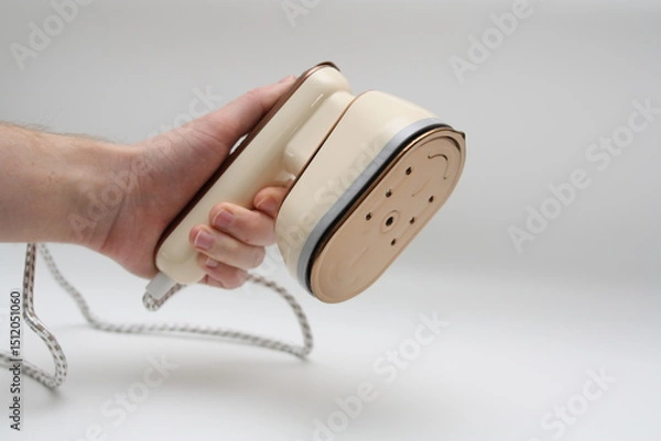 Obraz Male hand with a clothes steamer. Portable iron. Iron for ironing clothes. White background. Horizontal photo. There is space for text. Selective focus.