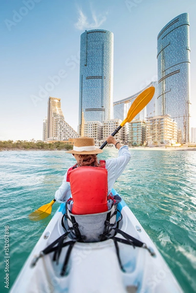 Fototapeta Tourist paddling a kayak in the calm waters in Abu Dhabi, United Arab Emirates, enjoying the scenic view of city skyline