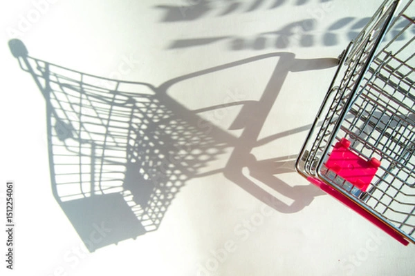 Fototapeta Shadow of a supermarket shopping cart on a white background with sunlight. Minimalist shopping concept.