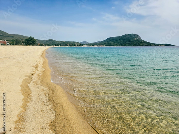 Fototapeta Yellow sand beach view with clear water and gentle waves under a blue sky in Toroni village on Sithonia peninsula, Greece