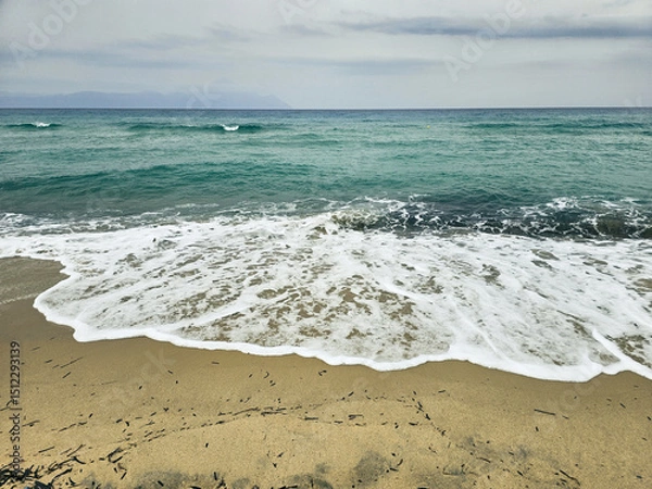 Fototapeta Calm sea waves gently lapping the shore on a cloudy day at the beach in Sarti on Sithonia peninsula, Greece
