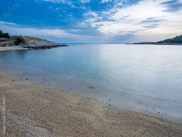 Fototapeta Tranquil beach with soft sand and calm water during twilight in a serene coastal landscape in Toroni on Sithonia peninsula, Greece