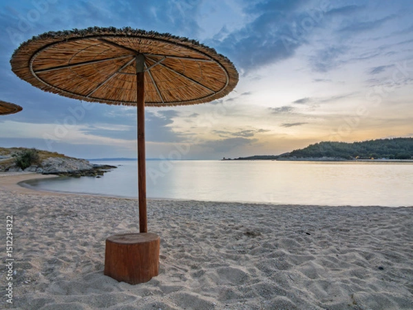 Fototapeta Serene beach with straw umbrellas at sunset in Toroni on Sithonia peninsula, Greece