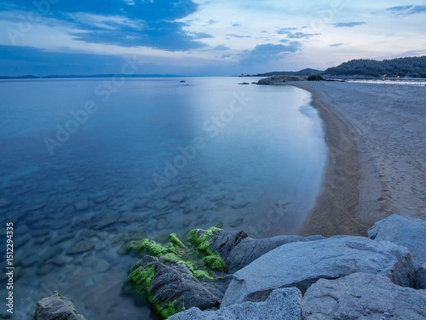 Fototapeta Calm evening at a coastal beach with smooth waves and rocky shoreline under a cloudy sky in Toroni on Sithonia peninsula, Greece