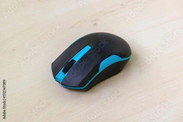 Fototapeta Bluetooth computer mouse, black and blue, on wooden surface. Cordless and user-friendly design for seamless computer navigation.