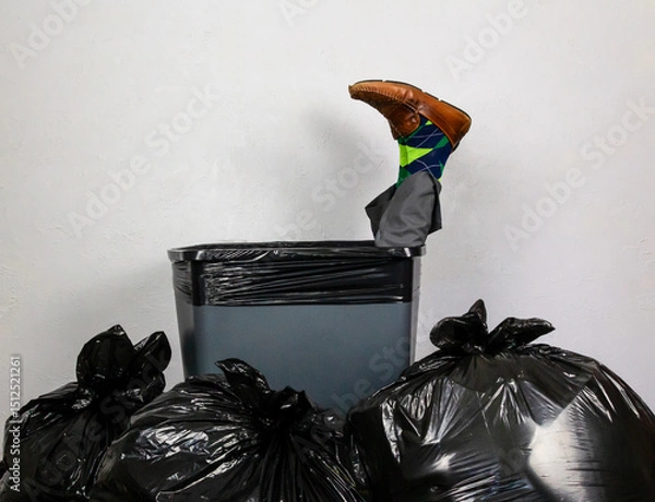 Fototapeta Businessman Stuffed in Trash Can Surrounded by Pile of Garbage Bags. Over a Barrel. Concept of Being Sacked or Fired.