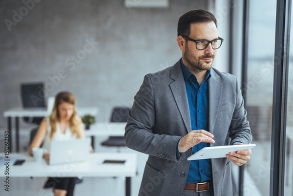 Fototapeta Confident Businessman Using Tablet in Modern Office with Colleague in Background