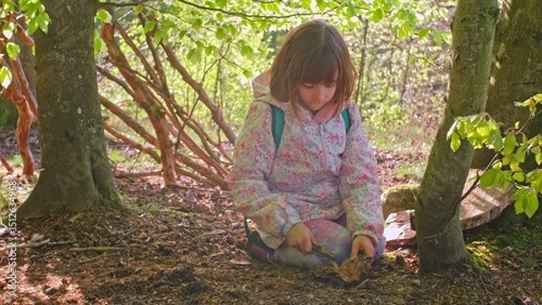 Fototapeta Smart Curious Caucasian Girl Playing in Forest with Piece of Wood Practicing Survival and Bushcraft Skills