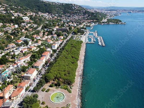 Fototapeta A stunning drone view of Trieste from Barcola, showcasing the city's coastline, historic buildings, and Adriatic charm under a clear northern Italian sky.