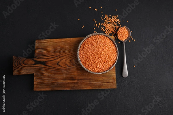 Obraz Red lentils on a ceramic plate on a wooden board on a black table, close-up, top view.