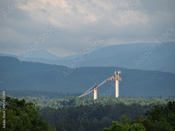 Obraz The Olympic Jumping Complex in Lake Placid, Upstate New York, lit by late evening sun rays, seen from afar with mountains in the background.