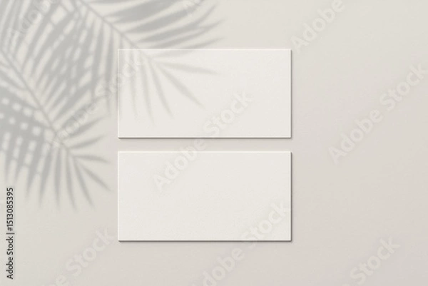 Fototapeta Blank Canvas: Two blank business cards sit on a light-colored surface, creating an illusion of depth and highlighting the soft shadows of tropical leaves.