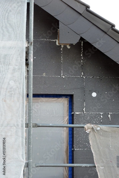 Fototapeta A wall of a house covered with EPS graphite polystyrene boards for thermal insulation, a window covered with a protective film, a scaffolding