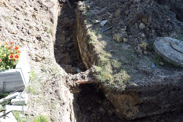 Fototapeta The deep ditch and a plastic orange pipe in marshy land next to a concrete cesspit to drain grounds, a hatch to a cesspit